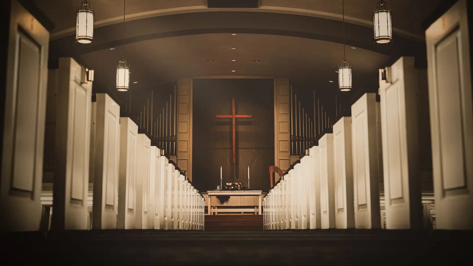 Church sanctuary interior with white pews, hanging lanterns, and a wooden cross above the altar