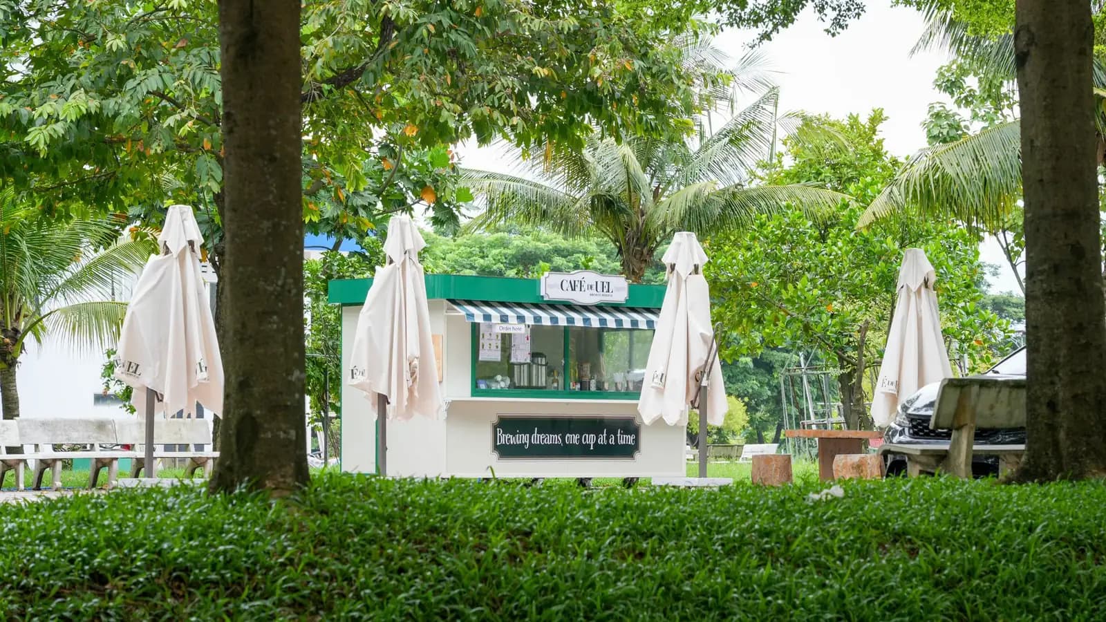 Small modern standalone coffee kiosk with a green awning and patio seating