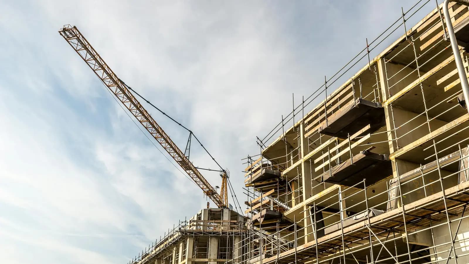 Commercial building under construction with a tall tower crane against a blue sky