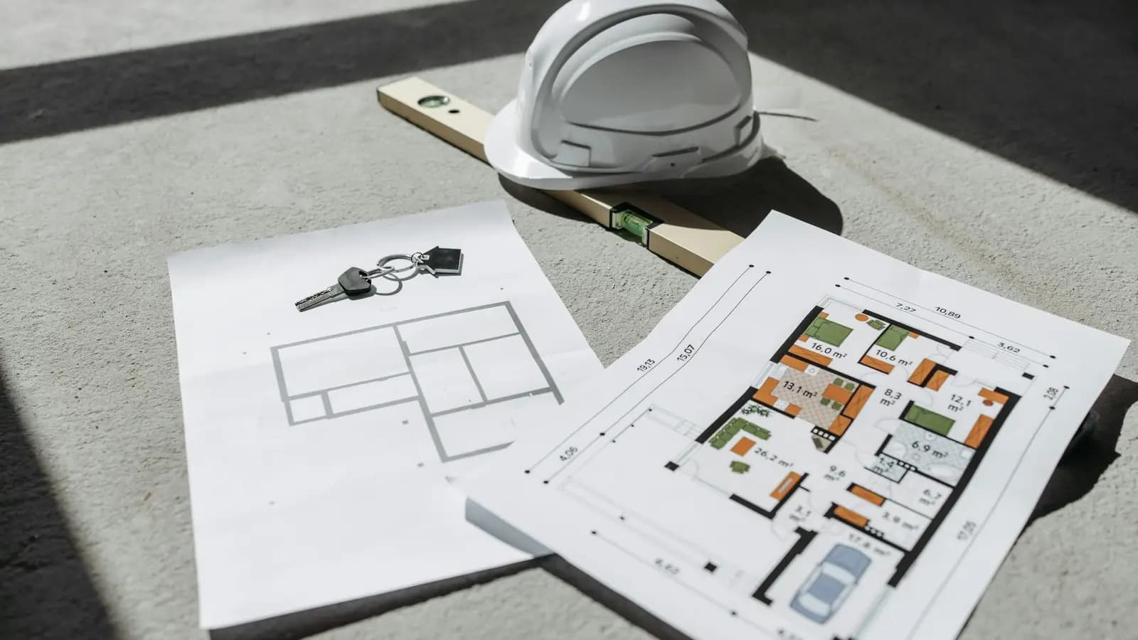 Construction floor plans, a hard hat, and a level laid out on a sunlit job-site floor