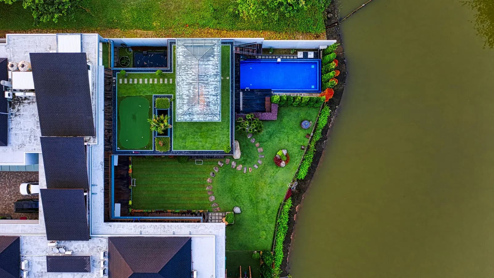 Aerial view of a landscaped lakefront yard with a manicured lawn, garden beds, and a stone path to the water