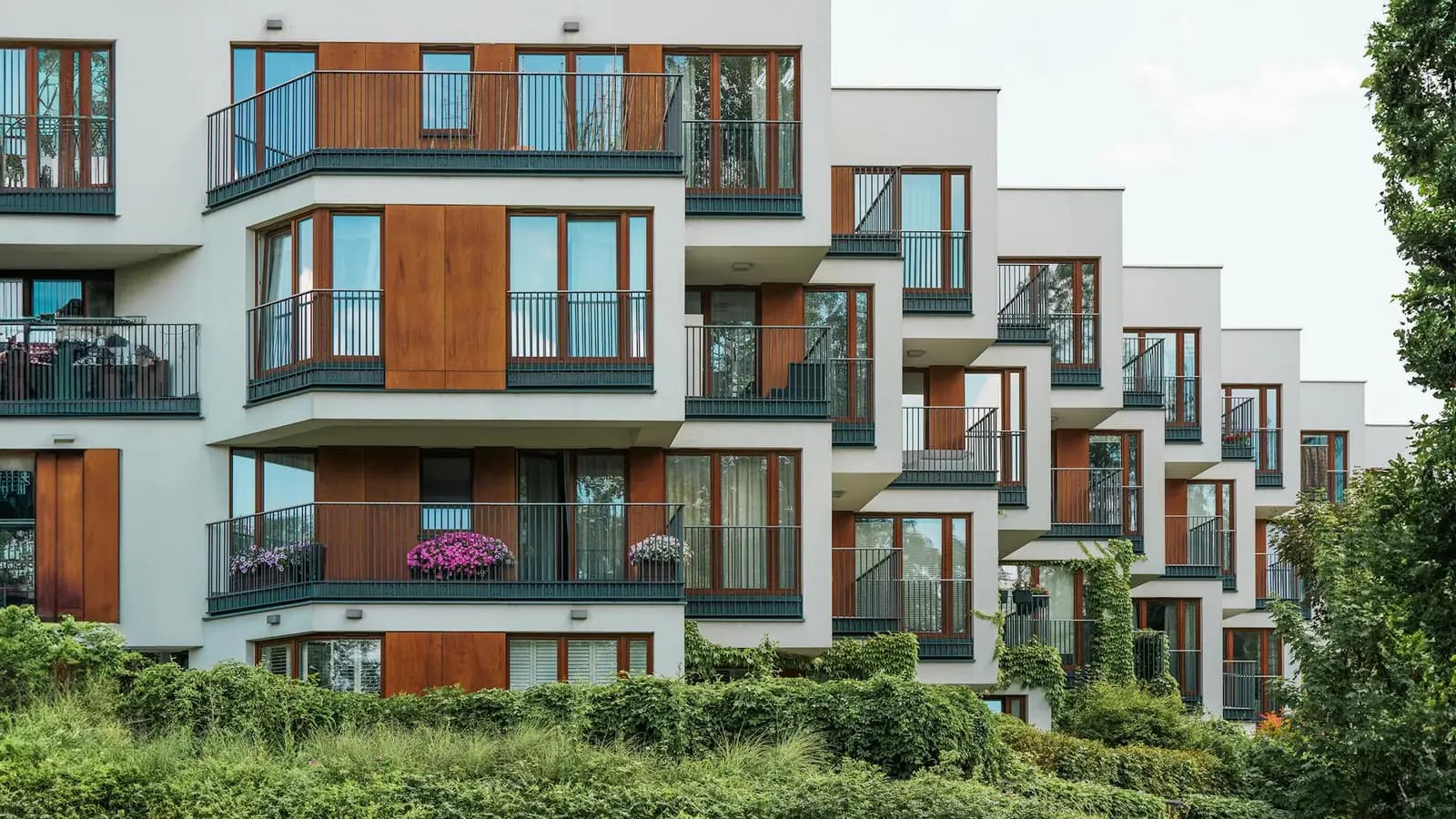 Modern multifamily apartment building exterior with wood-accent balconies and landscaped greenery