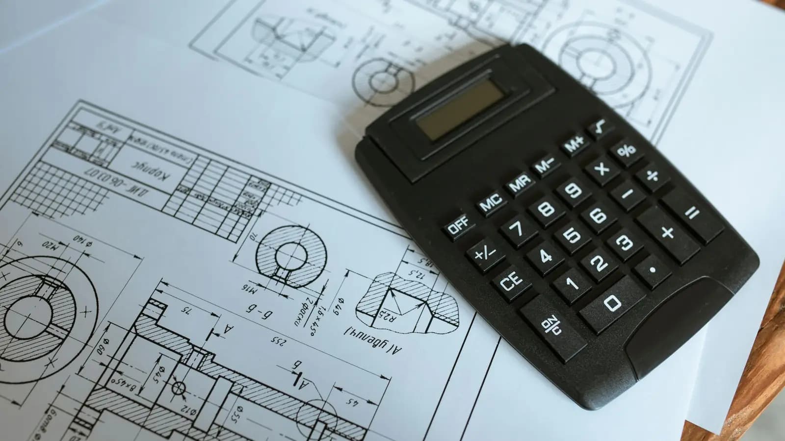 A calculator resting on detailed engineering blueprints and technical drawings